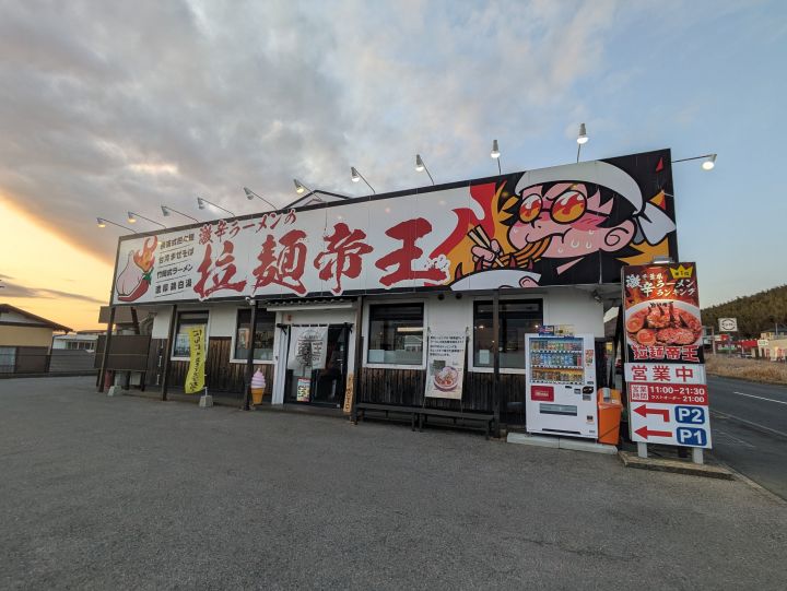 青空に映える激辛ラーメンの拉麺帝王君津店の赤い看板と店舗外観