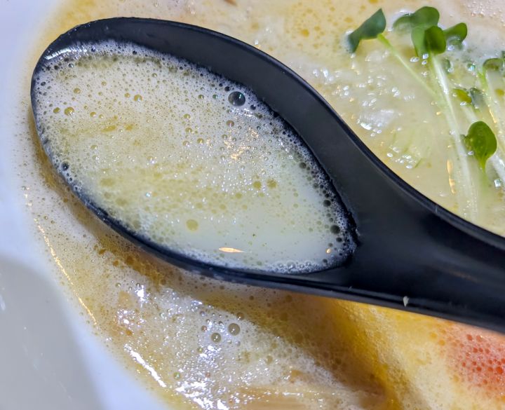 レンゲですくった濃厚でクリーミーな拉麺帝王の鶏そばの白湯スープ