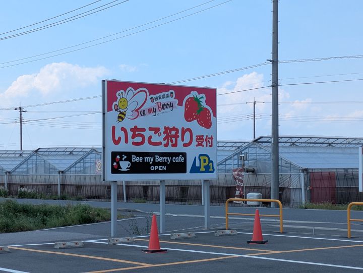 いちご狩りの受付看板と奥に並ぶビニールハウス