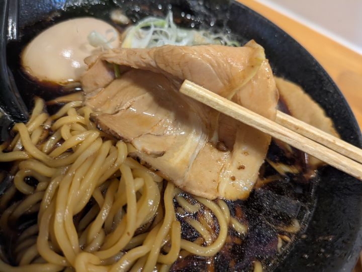 木更津ラーメン大輝のブラックラーメンの大きなチャーシューを箸で持ち上げた様子